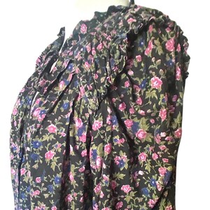 May include: A black floral print blouse with pink, blue, and green flowers. The blouse has a ruffled neckline and sleeves, and a tie detail at the neck. The fabric appears to be lightweight and flowy.