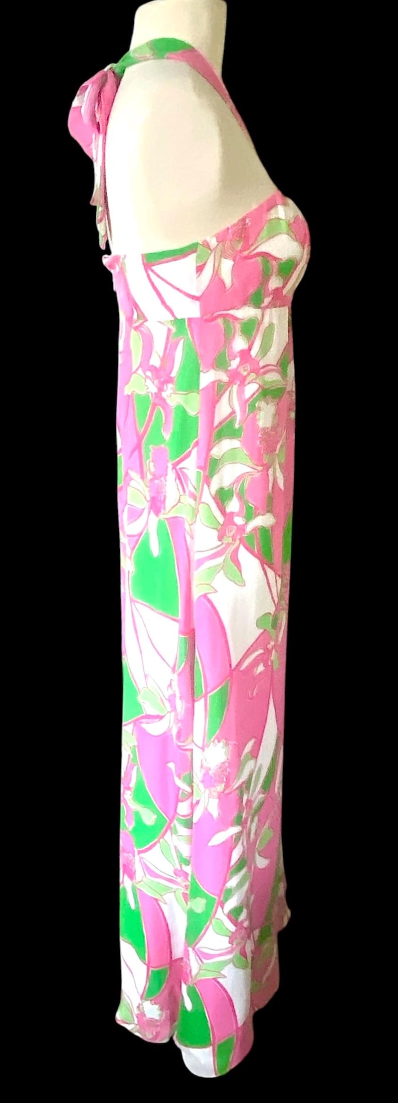 Op de afbeelding: Een lange halterjurk met een bloemenpatroon in roze, groen en wit. De jurk heeft een getailleerd lijfje en een zwierige rok. Perfect voor een zomerse gelegenheid.