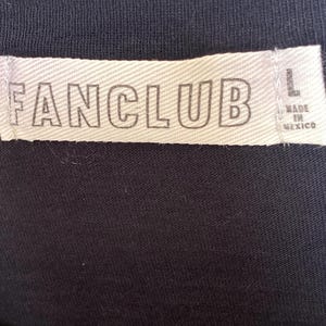 May include: Close-up of a black garment with a white tag. The tag reads "FANCLUB" in bold, capital letters. The tag also indicates the size "L" and "MADE IN MEXICO".