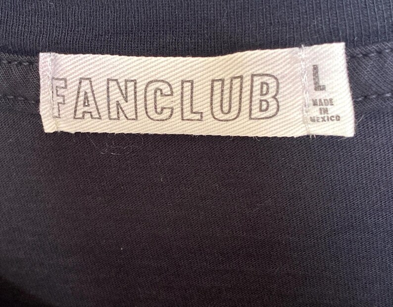 May include: Close-up of a black garment with a white tag. The tag reads "FANCLUB" in bold, capital letters. The tag also indicates the size "L" and "MADE IN MEXICO".