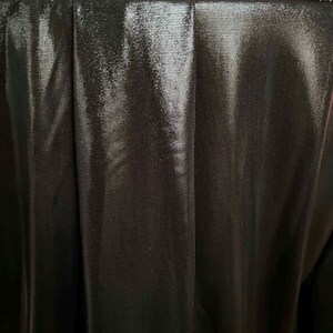 May include: Close-up of a black, shiny fabric with a pleated texture. The fabric has a subtle sheen and a smooth, soft feel.