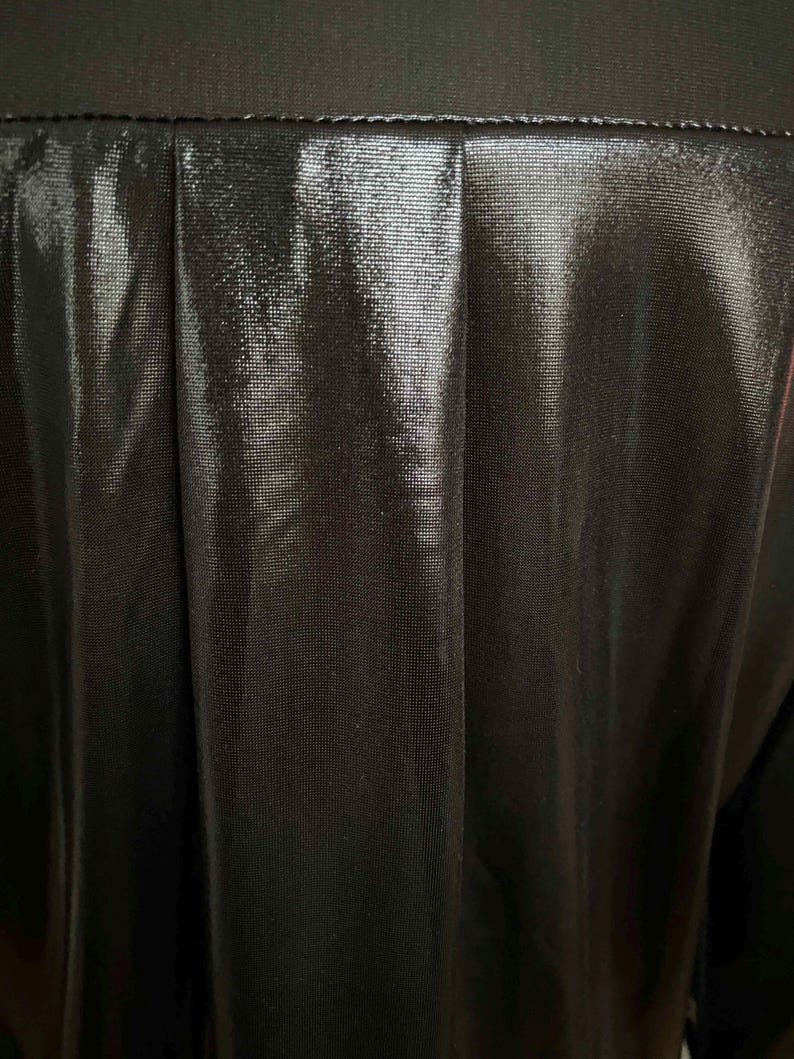 May include: Close-up of a black, shiny fabric with a pleated texture. The fabric has a subtle sheen and a smooth, soft feel.