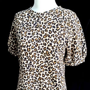 May include: A white short-sleeved shirt with a brown and black leopard print.