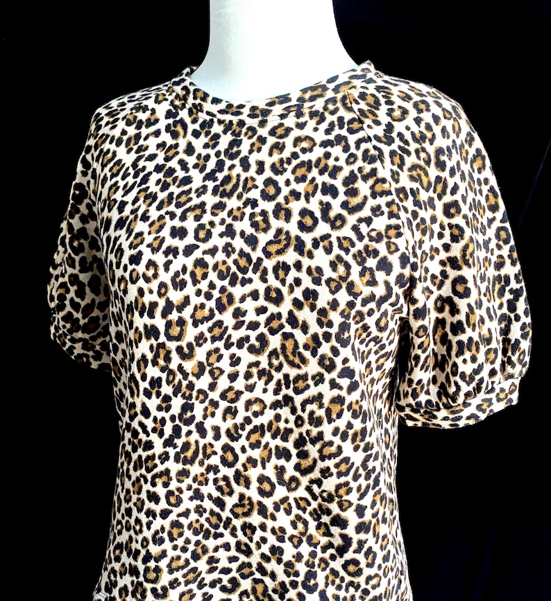 May include: A white short-sleeved shirt with a brown and black leopard print.