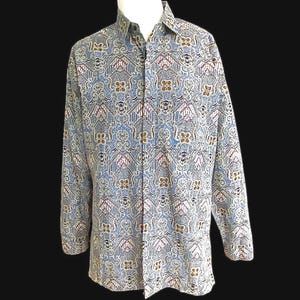 May include: A long-sleeved button-down shirt with a detailed, repeating pattern in shades of blue, brown, and burgundy. The shirt is displayed on a mannequin, showcasing its full length and design. The pattern features floral and geometric shapes.