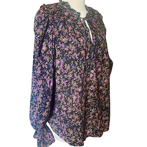 May include: A black floral blouse with a ruffled collar and long sleeves. The blouse features a pattern of small pink, blue, and green flowers. The sleeves have a ruffled cuff. The blouse has a button-down front and a tie at the neckline.