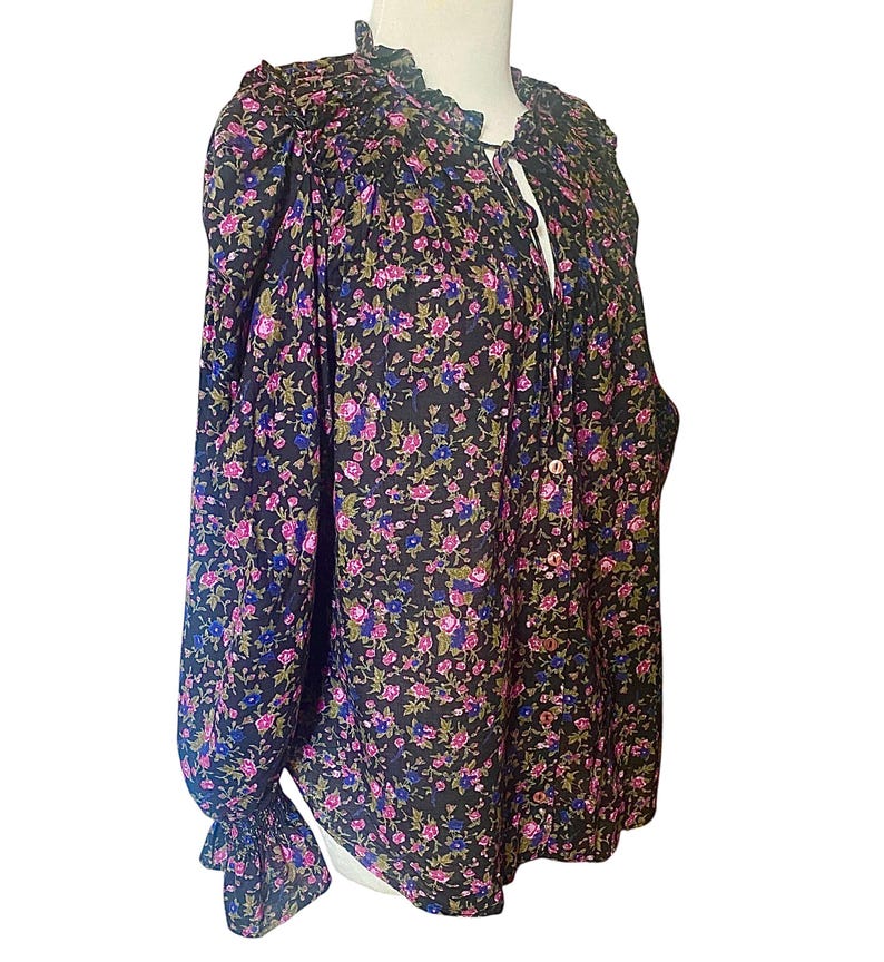 May include: A black floral blouse with a ruffled collar and long sleeves. The blouse features a pattern of small pink, blue, and green flowers. The sleeves have a ruffled cuff. The blouse has a button-down front and a tie at the neckline.