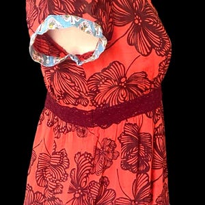May include: Coral-colored top with a dark brown floral pattern. The top features a V-neck, short sleeves with blue and white trim, and a burgundy lace waist. The bottom hem also has blue and white trim.