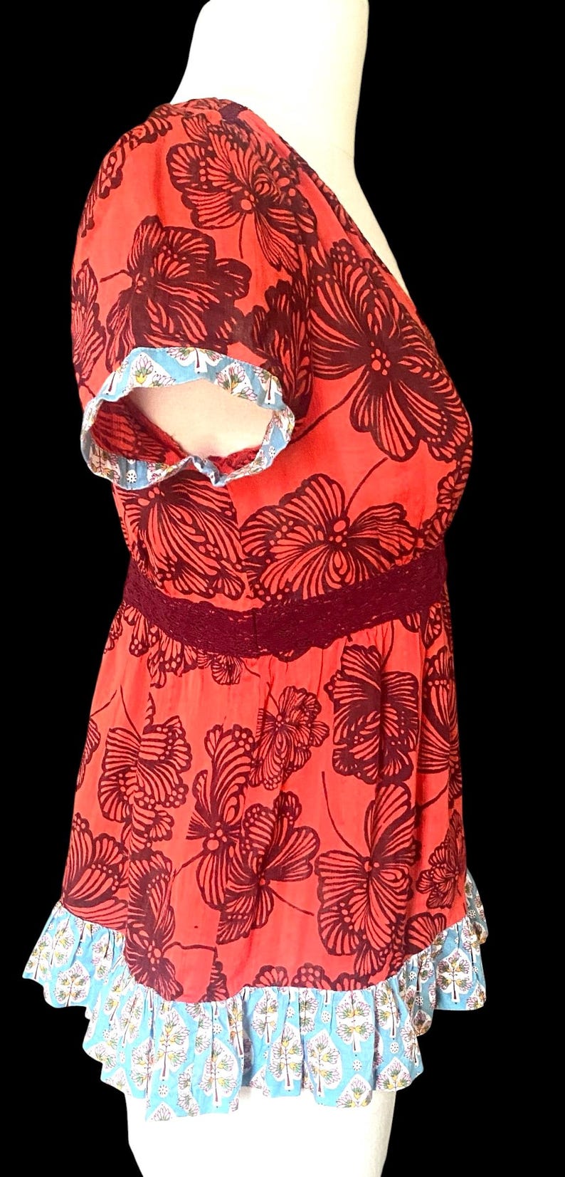 May include: Coral-colored top with a dark brown floral pattern. The top features a V-neck, short sleeves with blue and white trim, and a burgundy lace waist. The bottom hem also has blue and white trim.