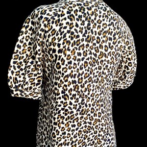 May include: A white, brown, and black leopard print short-sleeved shirt with a round neckline.