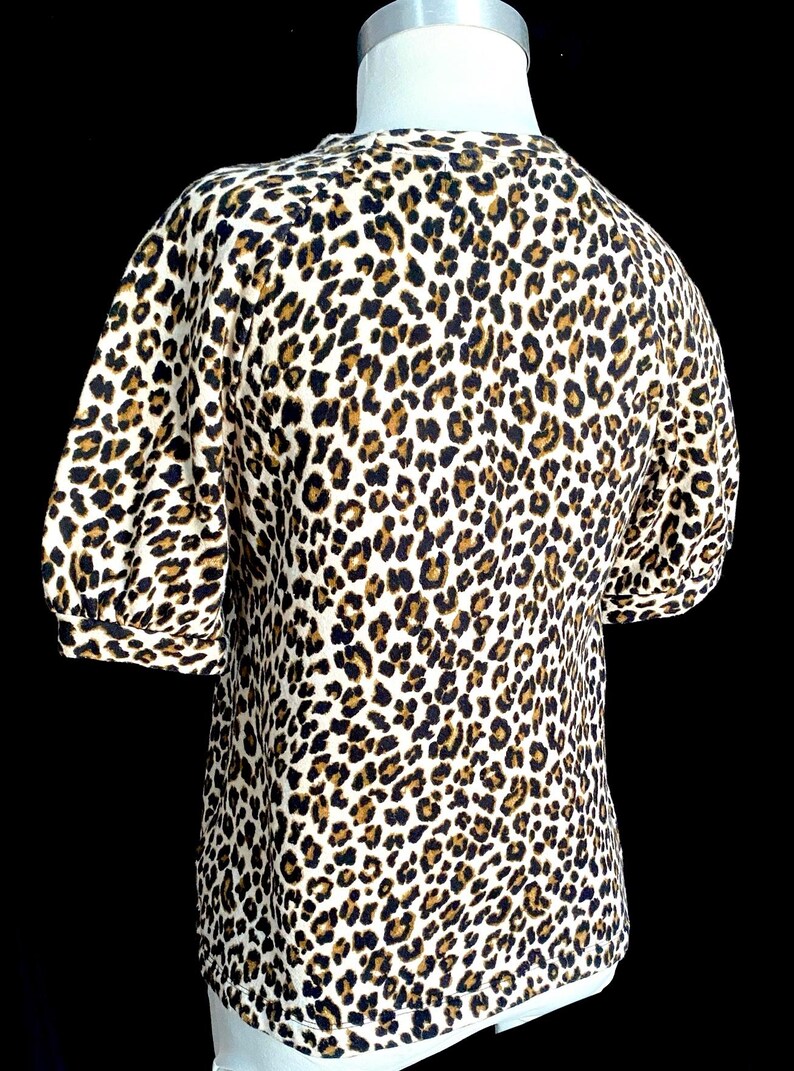 May include: A white, brown, and black leopard print short-sleeved shirt with a round neckline.