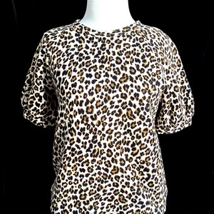 May include: A white short-sleeved shirt with a brown and black leopard print.