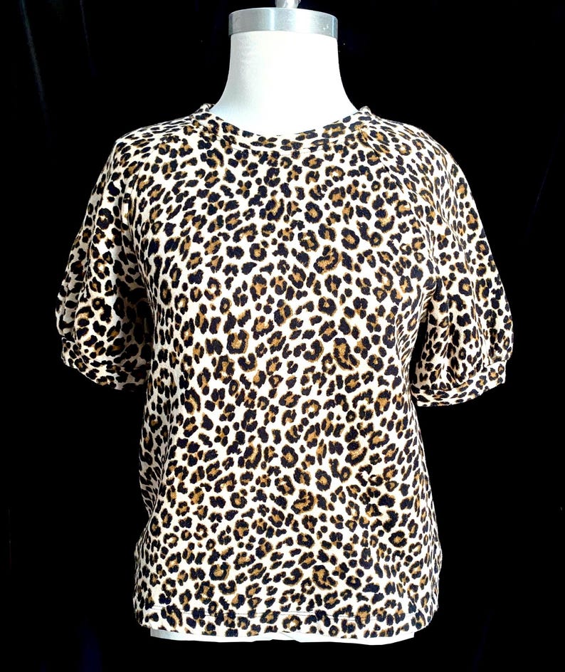 May include: A white short-sleeved shirt with a brown and black leopard print.