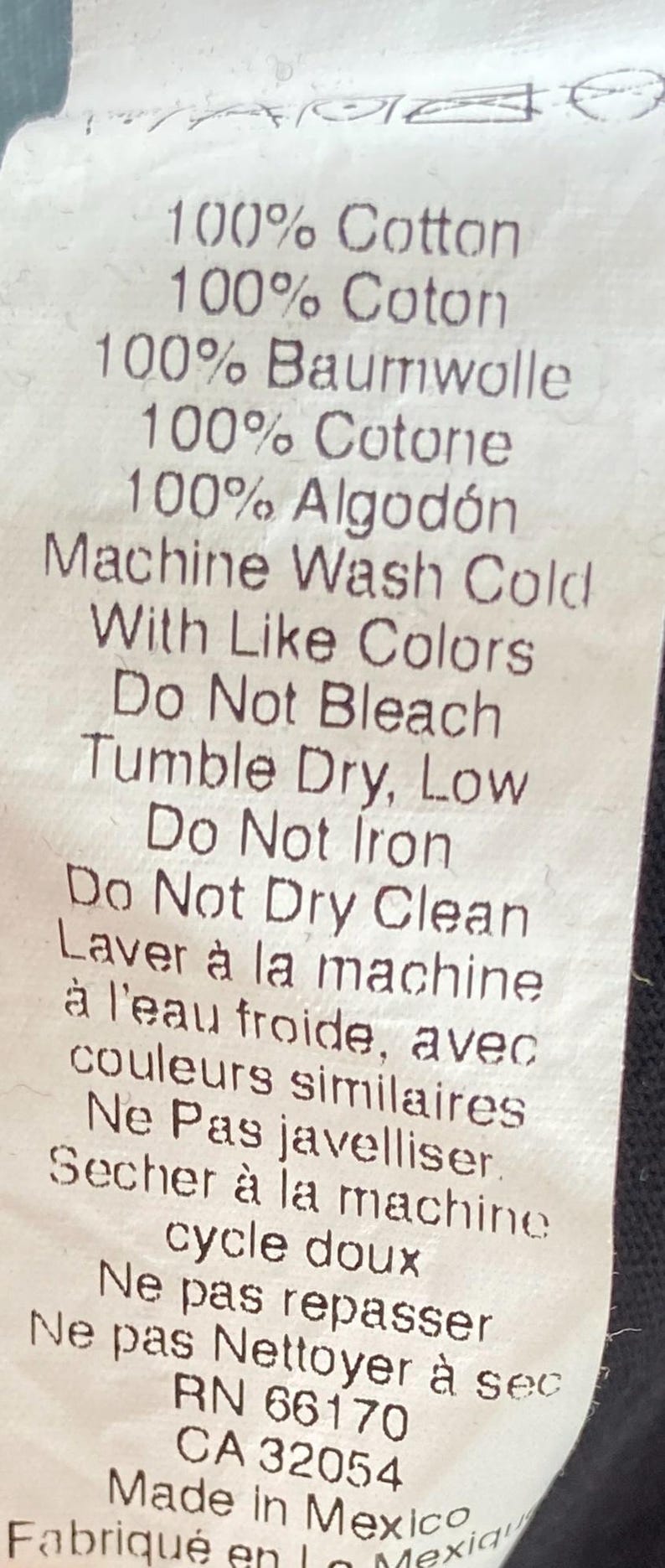May include: A white fabric tag with black text detailing fabric composition and care instructions. The tag lists 100% cotton in multiple languages, including English, French, German, Spanish, and Italian. Washing instructions are also provided.