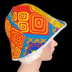 May include: A colorful bucket hat with a geometric pattern in red, orange, yellow, and blue. The hat has a white trim and a brim. The hat is on a mannequin head.