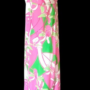 Op de afbeelding: Lange mouwloze jurk met een levendig bloemenpatroon in roze, groen en wit. De jurk heeft een halterhalslijn en een vloeiend silhouet. De stof lijkt lichtgewicht, geschikt voor warm weer.