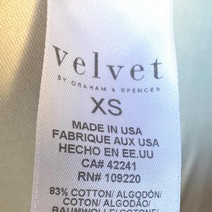 May include: White tag with black text that reads "Velvet by Graham & Spencer" and "XS". The tag also includes the following information: "Made in USA", "Fabrique aux USA", "Hecho en EE. UU", "CA# 42241", "RN# 109220", "83% Cotton/Algod&oacute;n/Coton/Algod&atilde;o/Baumwolle/Cotone/Katoen", and "17% Polyester/Poli&eacute;ster/Poli&eacute;ster/Nailon/Poliestere".