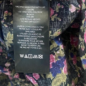 May include: Close-up of a black fabric with a floral pattern in pink, blue, and green. A black tag with white text details washing instructions: machine wash cold, non-chlorine bleach, line dry, low iron, and do not dry clean.