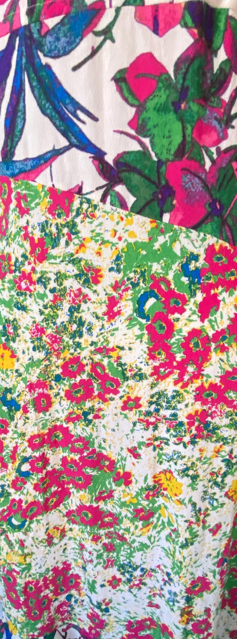 May include: Close-up of a fabric with a floral pattern. The design features a mix of pink, green, blue, and yellow flowers and foliage on a white background. The fabric has a vintage, hand-painted aesthetic.