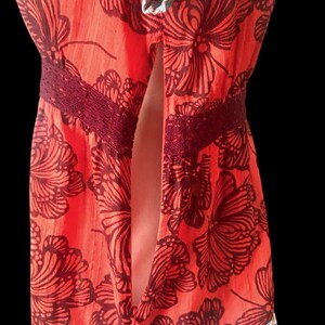 May include: A vibrant orange dress with a floral pattern in dark brown. The dress features a burgundy lace detail at the waist and a ruffled hem with a blue and floral print. The dress has a split front.
