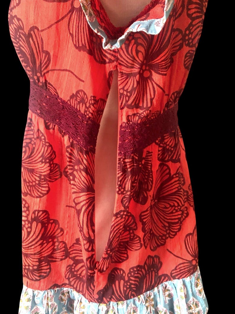 May include: A vibrant orange dress with a floral pattern in dark brown. The dress features a burgundy lace detail at the waist and a ruffled hem with a blue and floral print. The dress has a split front.