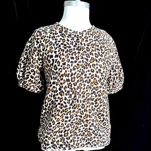 May include: A white short-sleeved shirt with a brown and black leopard print.