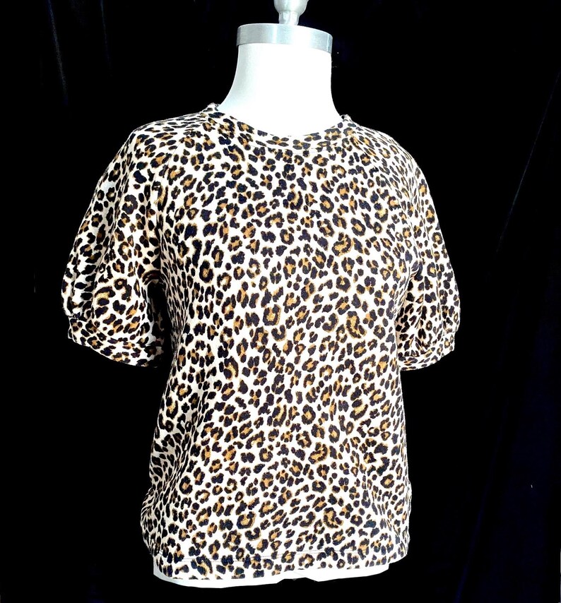 May include: A white short-sleeved shirt with a brown and black leopard print.