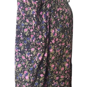 May include: A long-sleeved blouse with a floral pattern. The black fabric is covered in pink, blue, and green flowers. The blouse has a high ruffled collar and ruffled cuffs. The garment is displayed on a mannequin.