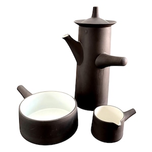 May include: A dark brown ceramic tea set with a tall teapot, a small creamer, and a serving bowl. The teapot has a lid and a spout. The creamer and bowl have white interiors and handles. The set is on a white background.