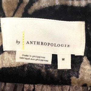 Puede incluir: Una etiqueta blanca con texto negro que dice "by ANTHROPOLOGIE" y "made in philippines/fabriqu&eacute; aux philippines". La etiqueta tambi&eacute;n tiene una etiqueta de talla que dice "M".