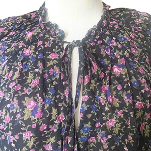 May include: A black floral top with a ruffled collar and a keyhole neckline. The fabric is covered in a pattern of pink, blue, and green flowers. The top is displayed on a mannequin.