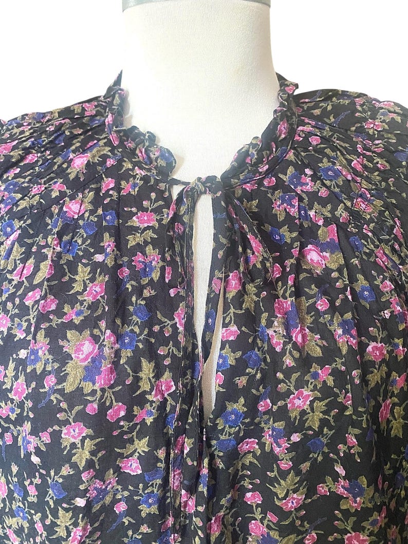 May include: A black floral top with a ruffled collar and a keyhole neckline. The fabric is covered in a pattern of pink, blue, and green flowers. The top is displayed on a mannequin.