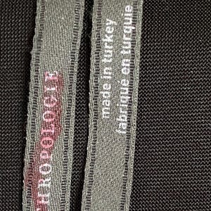 May include: A black fabric label with white text that reads "Made in Turkey, fabrique en turquie". The label also has the text "MANZERO ROGER" and "S" printed on it.