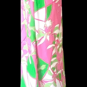 Op de afbeelding: Lange mouwloze jurk met een levendig bloemenpatroon in roze, groen en wit. De jurk heeft een halterhalslijn en een vloeiend silhouet. Het ontwerp bevat geometrische vormen en bloemmotieven.