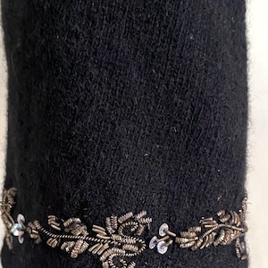 May include: Close-up of a black garment with a decorative trim. The trim features a floral design made of metallic wire and small, clear sequins. The fabric has a textured appearance.