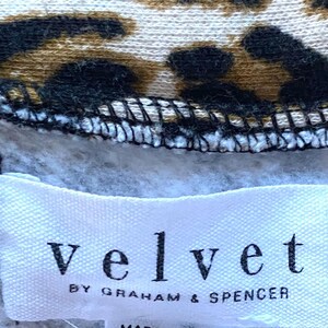 May include: A white tag with the text "velvet by graham & spencer" on a gray and brown leopard print fabric.