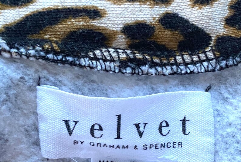 May include: A white tag with the text "velvet by graham & spencer" on a gray and brown leopard print fabric.