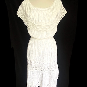 May include: A white, off-the-shoulder dress with a textured fabric and lace trim. The dress features a fitted bodice and a flowing skirt, perfect for a summer day. The dress is displayed on a mannequin against a black background.