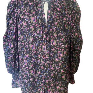 May include: A black floral print blouse with pink and blue flowers. The long-sleeved top has a ruffled collar and cuffs, and a button-down front. The blouse is made of a lightweight fabric.