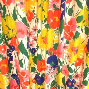 May include: A fabric featuring a vibrant floral pattern with a white background. The design includes large, colorful flowers in shades of bright yellow, orange-red, deep blue, and pink, interspersed with green leaves and stems throughout the textile.