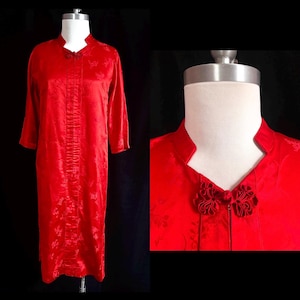 May include: A vibrant red, long-sleeved dress with a mandarin collar and decorative frog closures. The dress features a subtle floral pattern and is displayed on a mannequin against a black background. The dress is knee-length.