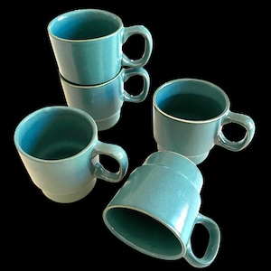 May include: A set of five turquoise ceramic mugs with rounded handles and a slightly flared shape. The mugs are stacked and arranged against a black background, showcasing their glossy finish and light-colored rims. The mugs are suitable for coffee, tea, or other beverages.