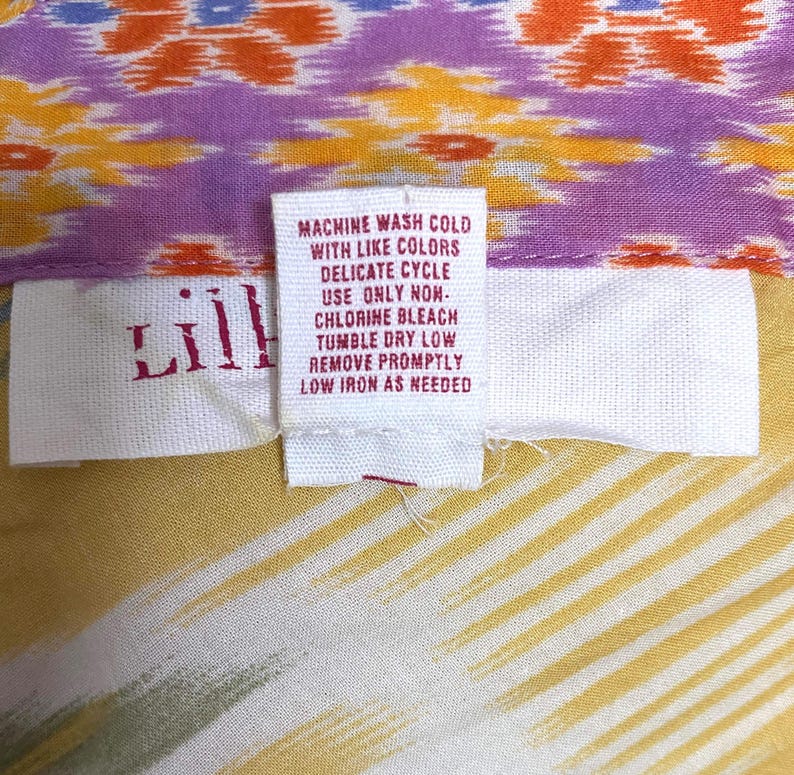 May include: Close-up of a colorful fabric with a tag. The fabric features a pattern of orange, purple, and yellow. The tag reads "Lill" and includes washing instructions: machine wash cold, delicate cycle, tumble dry low.