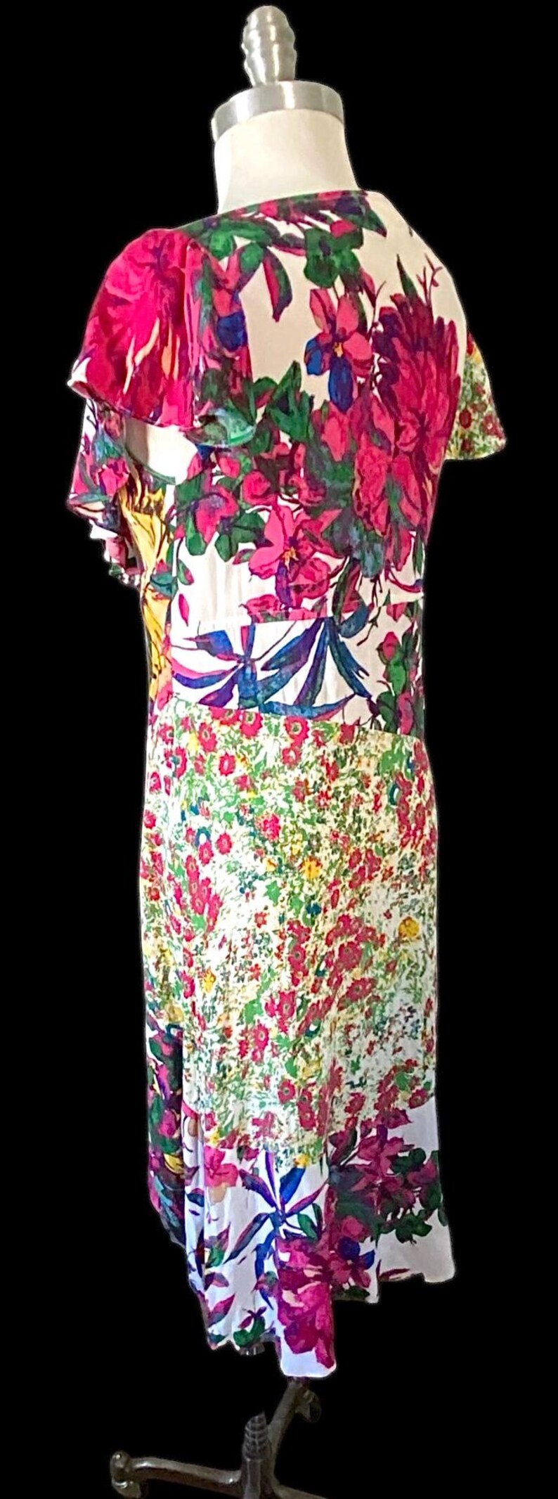 May include: A floral print dress on a mannequin. The dress features a white background with large pink, purple, and blue flowers. The dress has short sleeves and a knee-length hemline.