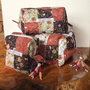 May include: Three patchwork fabric pouches in red, brown, and floral patterns. Each pouch has a zipper or a strap. The pouches are labelled "ISLAND STITCH Handmade in Tasmania". Small beaded keyrings are attached to the pouches.