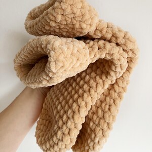 Pu&ograve; includere: Una morbida coperta di maglia beige con una texture soffice. La coperta &egrave; piegata a met&agrave; e sembra essere fatta di filato chenille.