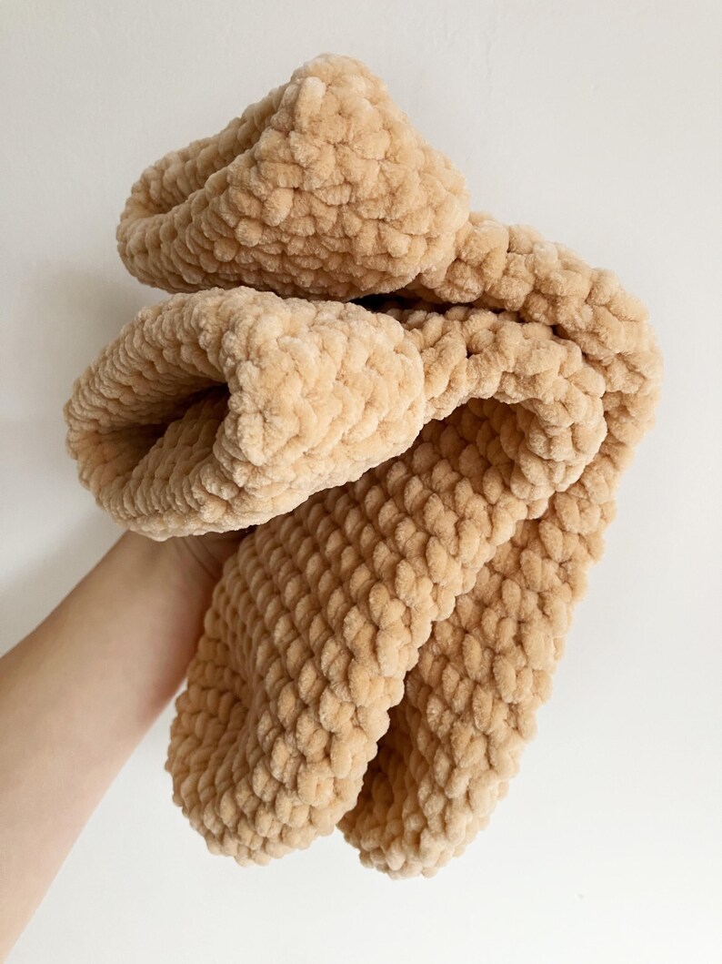 Pu&ograve; includere: Una morbida coperta di maglia beige con una texture soffice. La coperta &egrave; piegata a met&agrave; e sembra essere fatta di filato chenille.