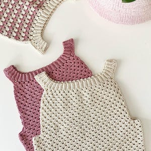 Può includere: Tre top all'uncinetto fatti a mano nei toni del rosa e del crema. I top presentano un motivo a punto strutturato e un design senza maniche. Un top ha un motivo a scacchi rosa e crema. I top sono esposti su una superficie bianca.