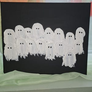 May include: A black canvas with a group of white ghost figures. Each ghost is painted with a textured, brushstroke effect, and has two small black dots for eyes. The artwork is a spooky, Halloween-themed piece.