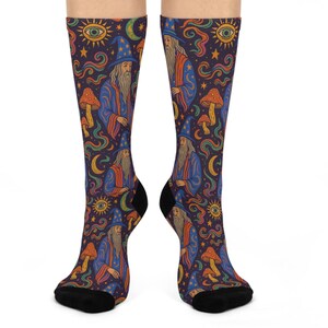 Puede incluir: Calcetines hasta la rodilla con un patrón repetido de un mago con túnica y sombrero azules, setas, ojos, estrellas y lunas crecientes sobre un fondo morado oscuro. Los calcetines tienen punteras y talones negros.